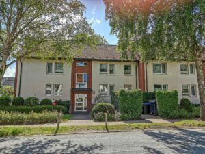 Ansicht auf Eingangsbereich eines Mehrfamilienhauses mit Putzfassade und Hecke/Bäume davor.